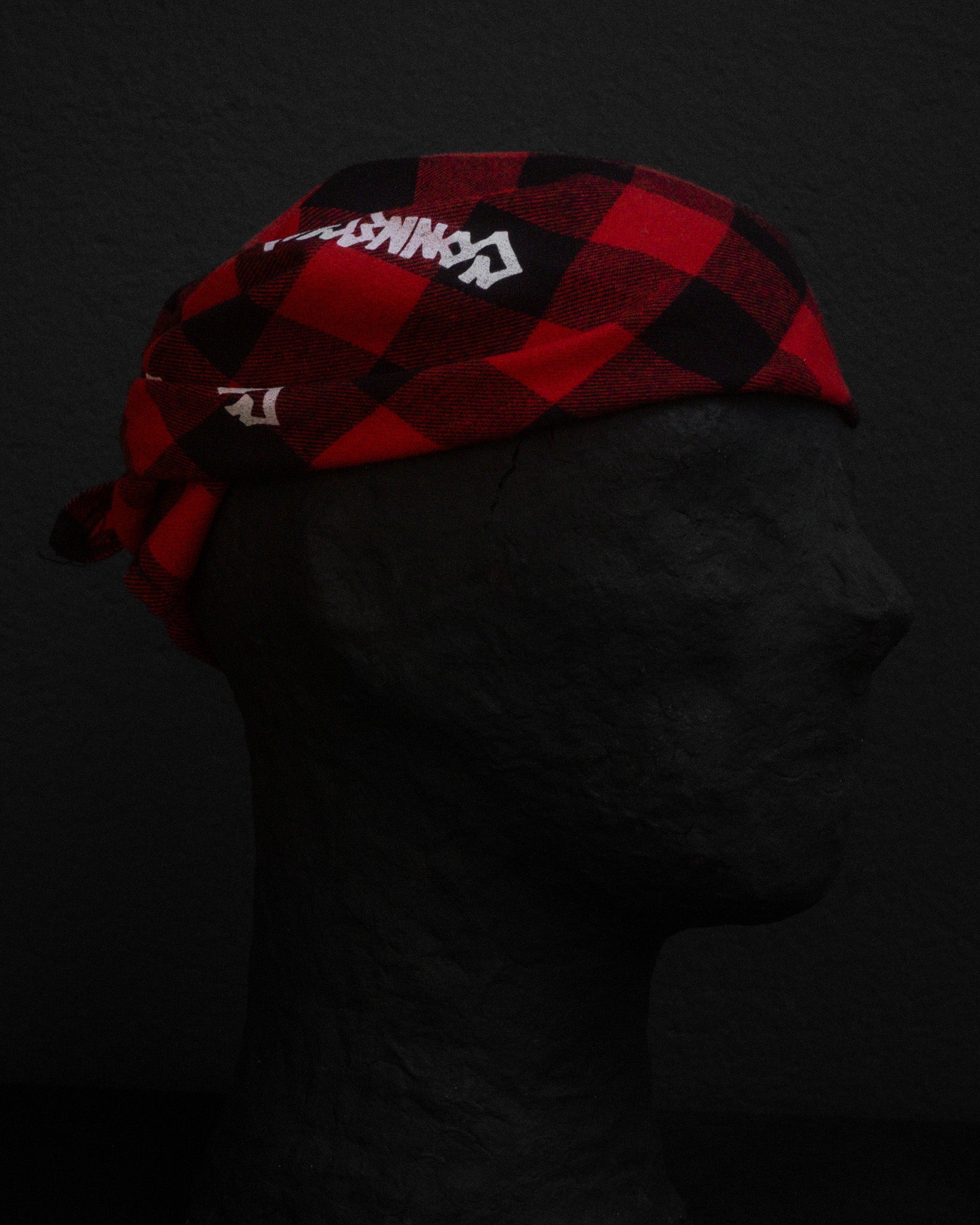 Red and black checkered bandana with branding on a dark background