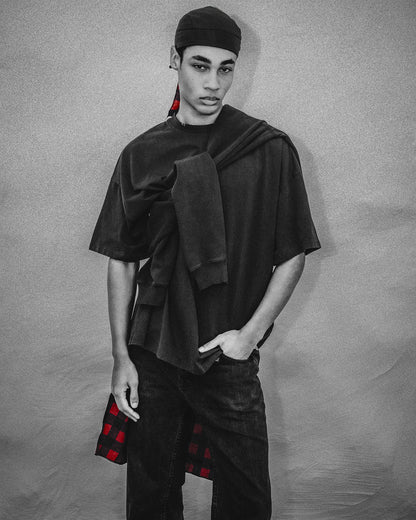 Person wearing a unique outfit with layered black garment against a plain background
