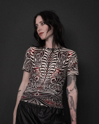 A model wearing Jean Paul Gaultier Cyberbaba 1996 tribal tattoo tee in off-white with black and red print